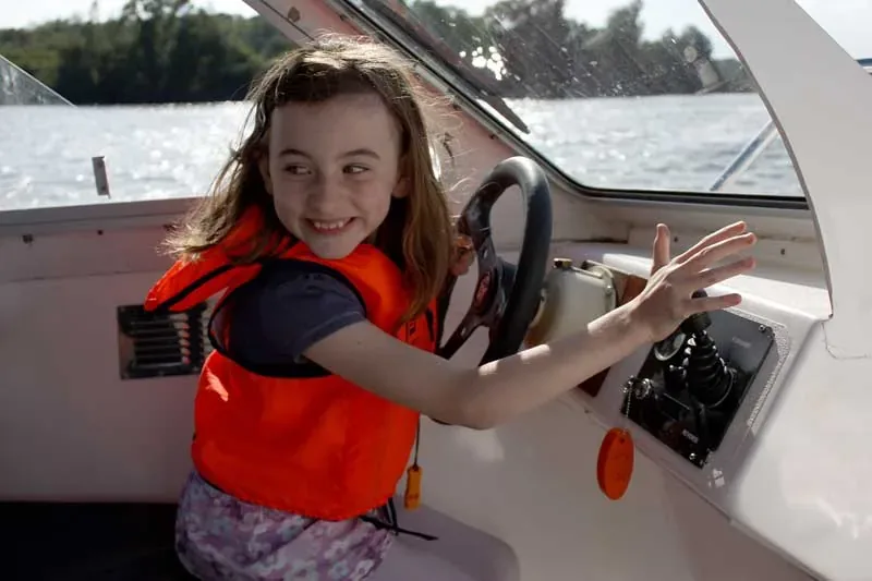 A child at the wheel of a boat, wearing a life jacket